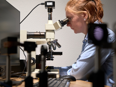 Montana State University senior Katerina Shabalin examines an optical fiber with a 3D printed lens using a microscope at Spectrum Lab